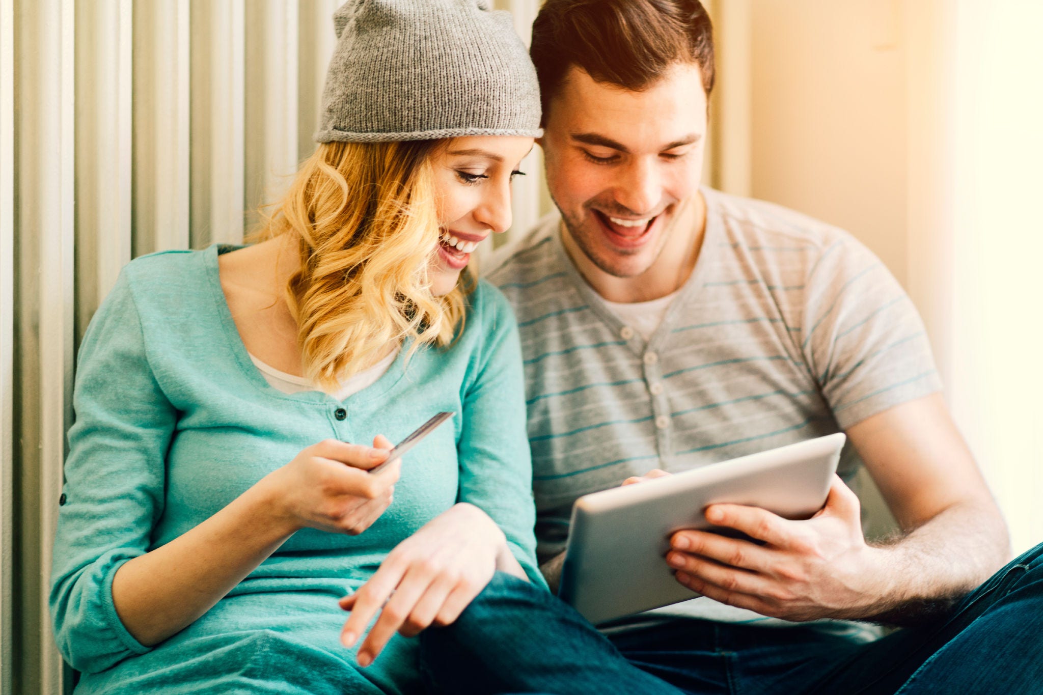 Young cheerful couple sitting on the floorand shopping online using digital tablet. Woma with hat holding credit card